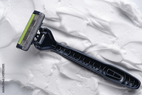 Black disposable razor on white shaving foam background.