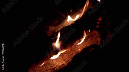 A log slowly burns in a dark night, flames dancing along its surface, creating a warm and mesmerizing glow. Perfect for projects related to nature, camping, or relaxation.