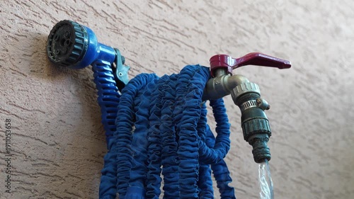 Water flows from the tap. Video with sound. Water tap outside the building. An outdoor tap for watering a garden plot. Blue hose with a watering nozzle is hanging on the tap
