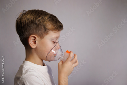 A cute boy wearing a nebulizer mask during an inhalation procedure. Child care and treatment of respiratory diseases at home.