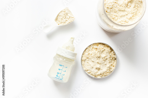 Baby milk bottle and powdered infant formula in the jar and scoop on white background. Top view.