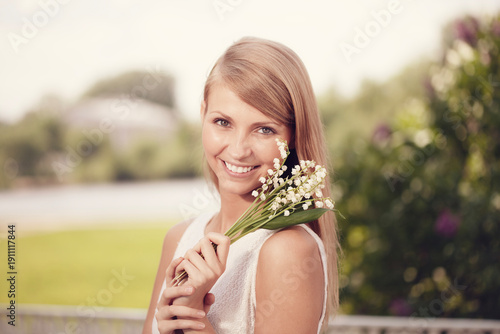 A woman presents a bouquet of lilies of the valley against a softly blurred natural backdrop.