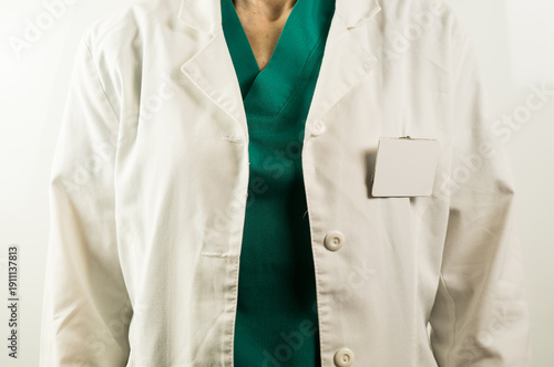 Fotografi A close-up shot of a medical professional wearing a white clinical coat over green hospital scrubs with a blank identification badge