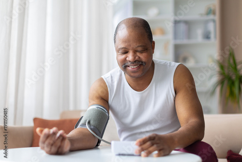 фотографія Mature black man checking blood pressure at home with digital monitor, smiling calmly