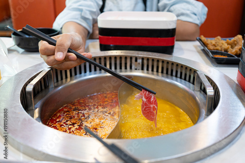 Hand holding raw sliced pork using chopsticks on hot pot with smoke for China hot pot also known as Shabu Shabu or Sukiyaki is Chinese style.