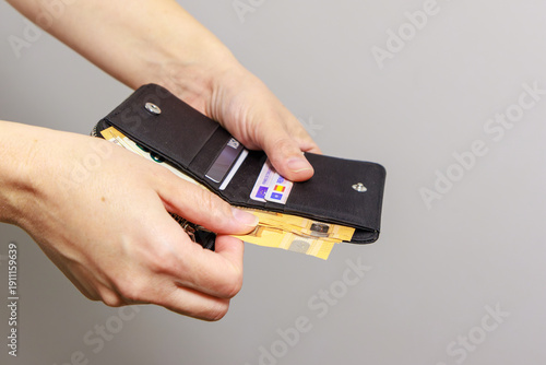 A person holds an open black wallet while taking out several euro banknotes. Inside, cards and organized compartments are visible. The banknotes appear to be 50 euro notes .