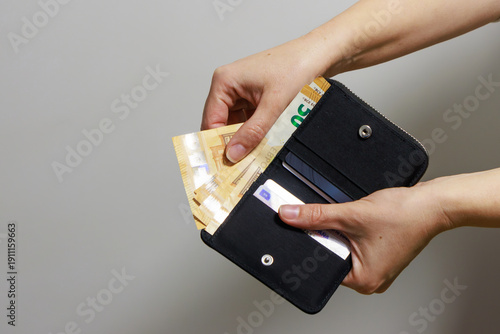 A person holds an open black wallet while taking out several euro banknotes. Inside, cards and organized compartments are visible. The banknotes appear to be 50 euro notes .