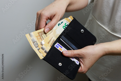 A person holds an open black wallet while taking out several euro banknotes. Inside, cards and organized compartments are visible. The banknotes appear to be 50 euro notes .