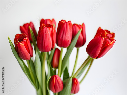 Bright red tulips arranged in a bouquet with green leaves against a plain white background, showcasing their vibrant color and natural beauty