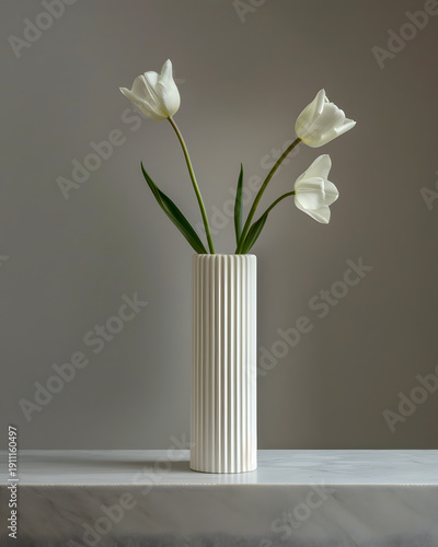 White tulips with green leaves arranged in a vertical ribbed vase on a marble surface against a soft gray background, showcasing modern floral decor