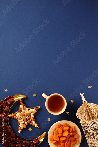 Ramadan food background with top copy space. Vertical composition featuring dates, nuts, dried fruits, and Arabic lantern on dark blue surface. Ideal for festive greeting cards.