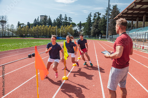 Athletes performing agility training on a running track with a coach using a digital tablet