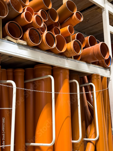 Cuadro en lienzo Large group of orange plastic sewer pipes stored on metal racks in a construction materials store or industrial warehouse