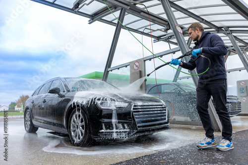 Foto Man washing black car with high pressure washer at self service car wash station outdoors