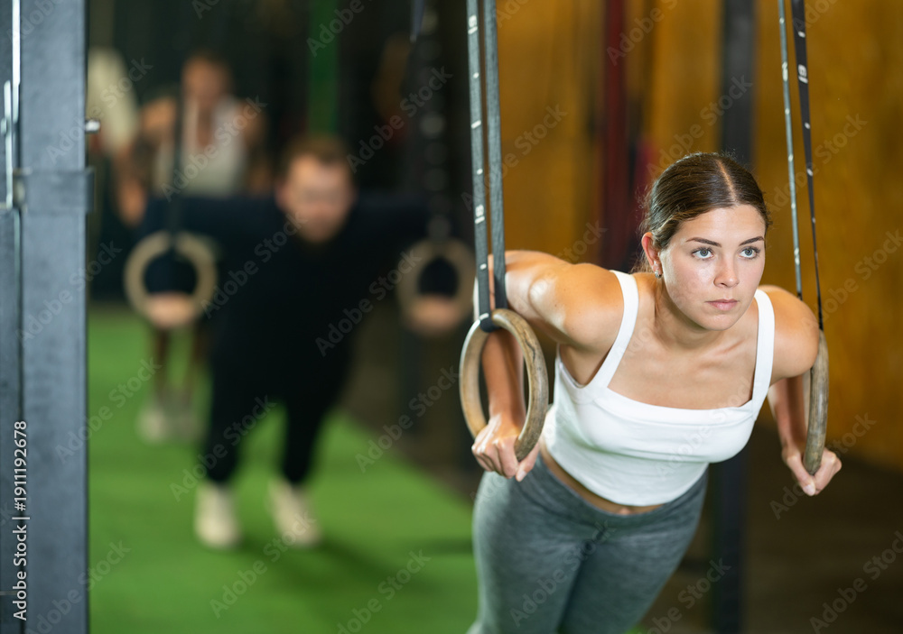 Obraz premium Determined young girl working out with gymnastic rings in gym during weight training classes