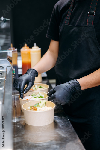 Chef assembling takeaway salad bowls in commercial kitchen, close up