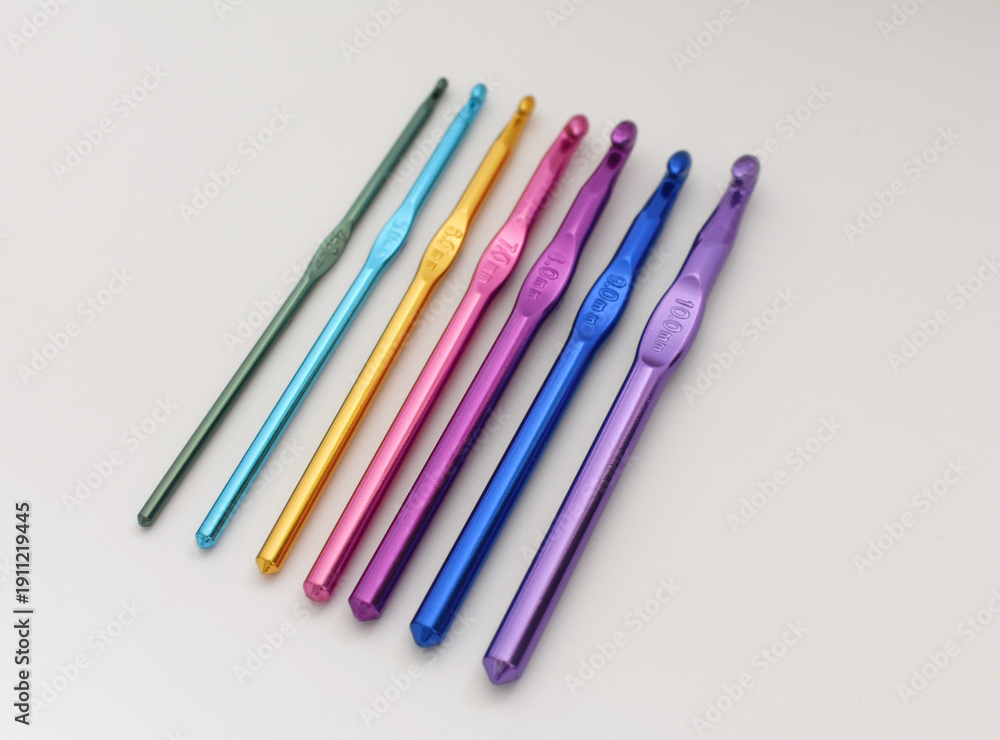 Fototapeta premium Top view of colorful crochet hooks arranged in a row. Creative DIY and craft concept for knitting, crochet projects, and handmade hobbies. 