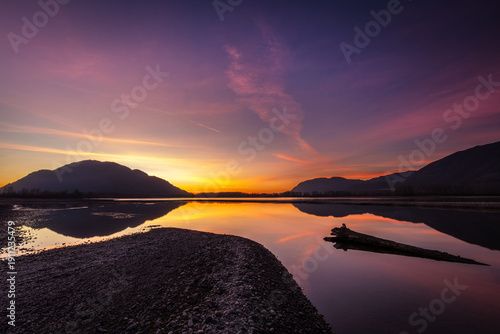 Colorful Sunset Reflection Over Fraser River with Driftwood and Mountain Silhouettes in Chilliwack British Columbia Canada