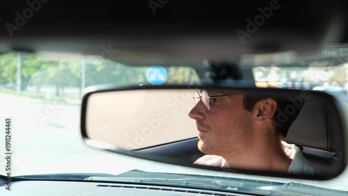Canvastavla Happy young male driver in glasses carefully looking at the road in the city and looking in the rear view mirror