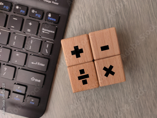 Wooden cubes displaying basic mathematical operator symbols arranged on a surface next to a computer keyboard