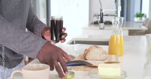 Hand reaching from left, opening jar, scooping and spreading jam on toast on counter for breakfast