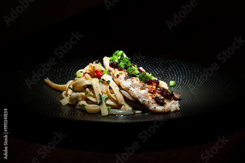 Spagetti aglio olio z kurczakiem w sosie śmietanowym na czarnym talerzu stojącym na stole