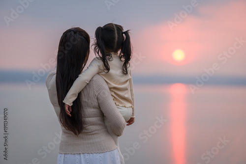 Loving mother holding child girl while watching the sunset glow