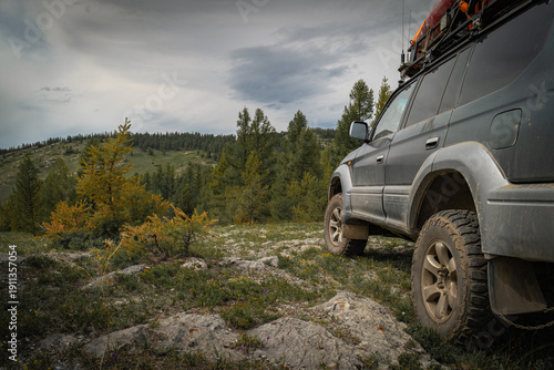Off-road vehicle on rocky mountain trail in Mongolia, close up of SUV wheels on rough terrain, expedition car in autumn forest under cloudy sky, adventure travel and 4x4 concept