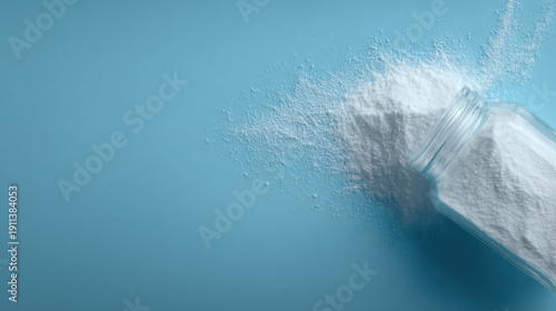Overhead shot of fine white powder gently spilling out from an overturned glass jar, creating a soft, scattered pattern on a serene blue surface, perfect for clean and abstract design concepts