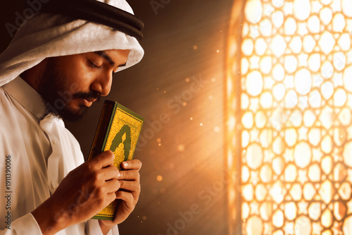 Young asian muslim man with beard holding holy book quran in the mosque window arch, eid adha mubarak concept