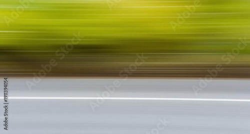 A fast moving car creates a dynamic motion blur as it travels down the asphalt highway under a bright sky, blending nature and transportation into a design of light and green texture lines
