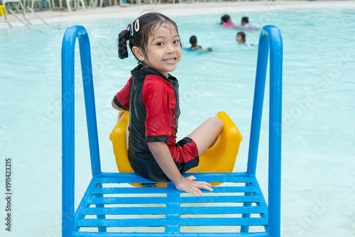 Asian girl playing on a slide in a pool.