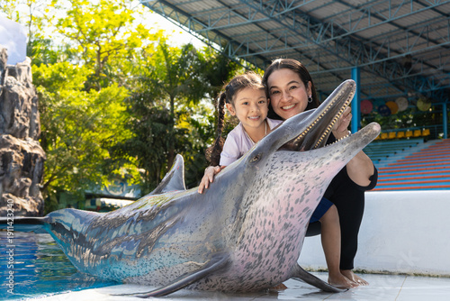 Asian mother and daughter take pictures with smiling dolphins while touring an amusement park.