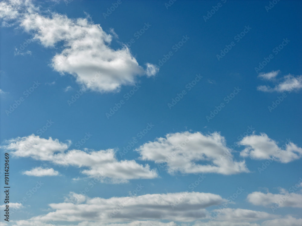 Obraz premium Blue sky displaying scattered white cumulus clouds, creating a vibrant backdrop for outdoor scenes and representing concepts of freedom, nature, and clear weather