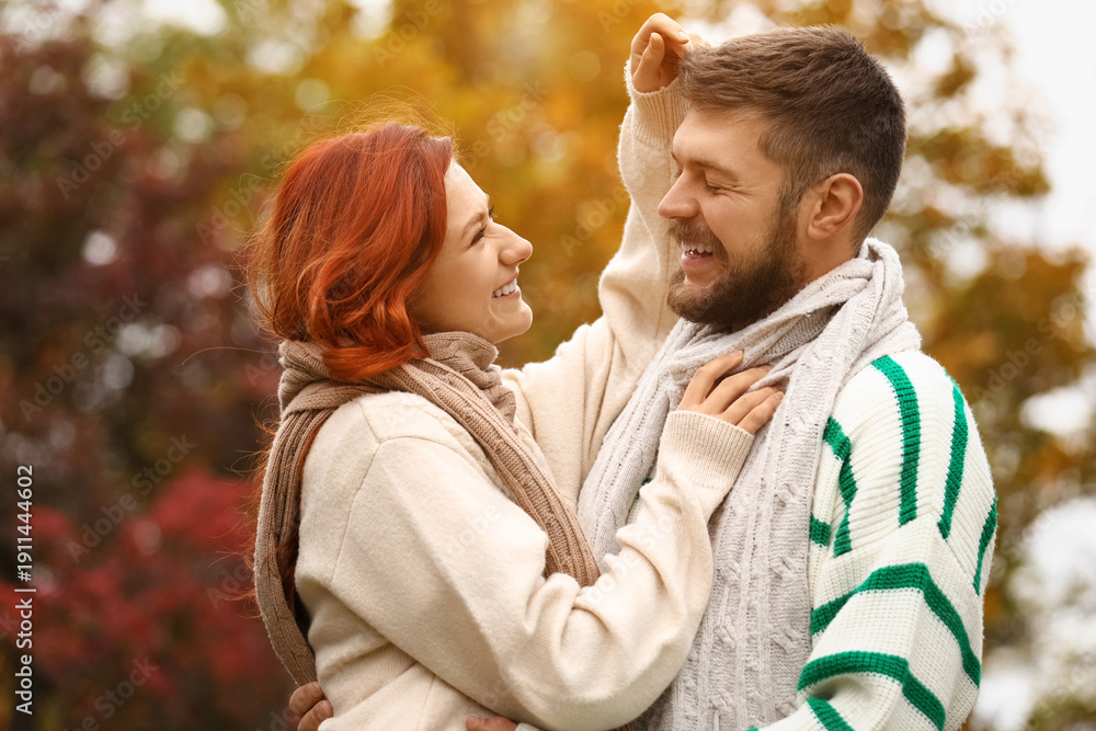 Fototapeta premium Cute young couple in warm sweaters and scarves hugging at autumn park