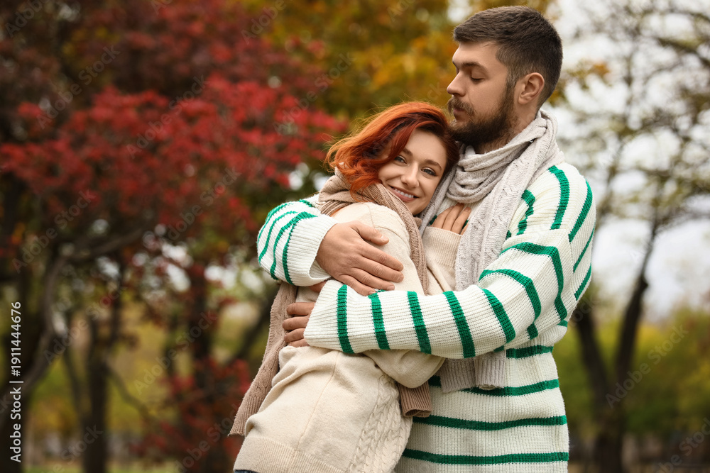 Fototapeta premium Cute young couple in warm sweaters and scarves hugging at autumn park