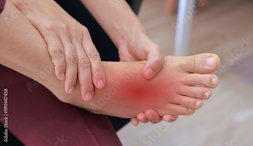 Woman massaging her painful foot with red highlight on sole and instep. Foot pain, plantar fasciitis, muscle strain, gout and peripheral neuropathy concept for health care and physical therapy.