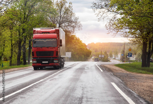Wallpaper Mural Red semi-truck travels on wet asphalt road lined with lush green trees on a cloudy spring day with a tractor parked roadside Torontodigital.ca