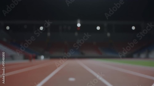 Empty athletic track in a large stadium at night with blurred lights and empty stands