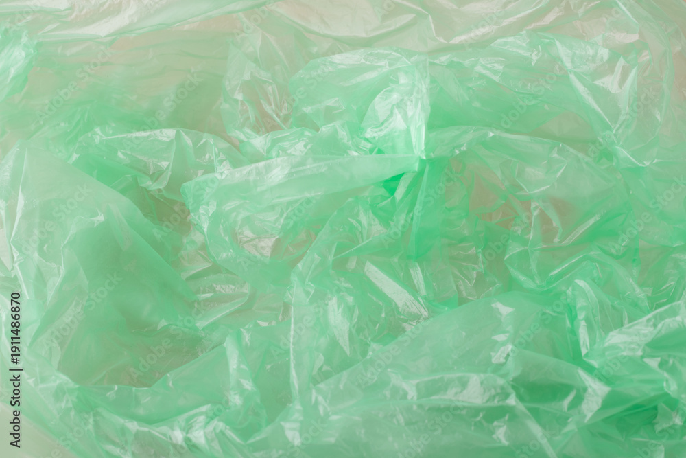 Obraz premium Crumpled green plastic material forming an abstract background texture. Showing translucent, synthetic, and reusable plastic packaging