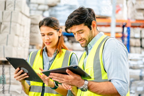 Foto Diverse team of warehouse supervisors in safety vests using digital tablets to m