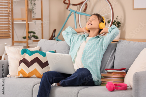 Happy teenage Asian girl in headphones with laptop and books sitting on onlin...