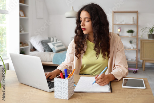 Teenage girl studying with laptop at table in bedroom