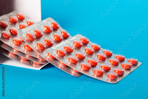Red anti-inflammatory tablets in packaging on blue background, close-up. Copy space for text, nonsteroidal