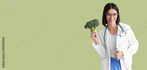 Female nutritionist holding broccoli and meal plan on green background with s...