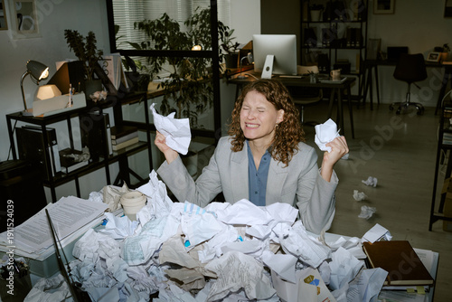 Foto Caucasian young woman sitting at cluttered office desk holding crumpled papers i