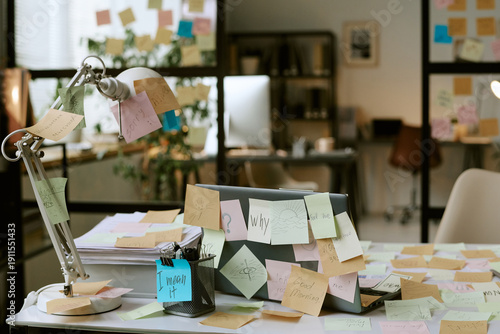 Office desk covered with colorful sticky notes surrounding closed laptop and desk lamp, business workspace showing brainstorming process and creative planning in modern office environment