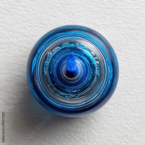 Blue bottle with a pointed tip sits on a white surface surrounded by an empty space