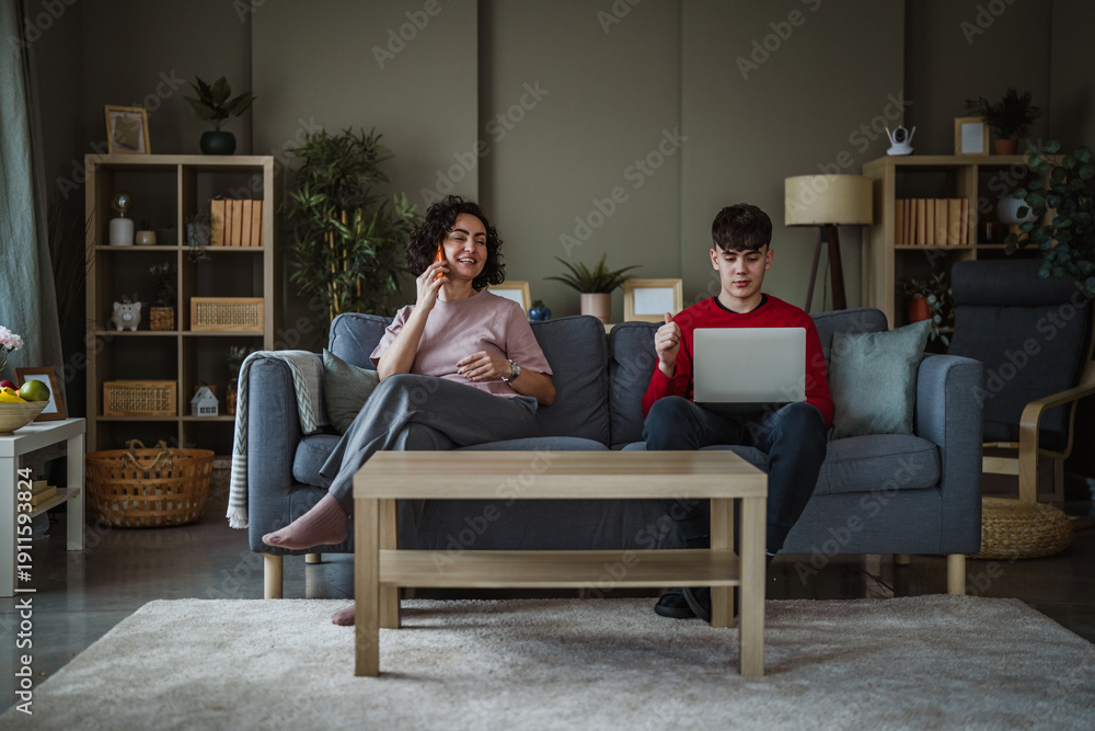 Obraz premium Mother and teenage son using devices on sofa