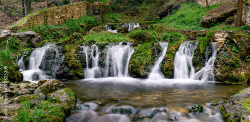 Panoramic long exposure of a cascading waterfall over mossy rocks in a lush green forest in Orbaneja del Castillo, Spain
